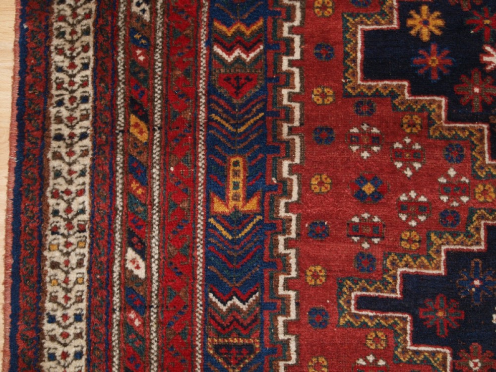 A hand-knotted antique Persian Afshar rug featuring three stacked diamond medallions surrounded by geometric floral motifs in navy blue, terracotta red, and ivory tones. View IV