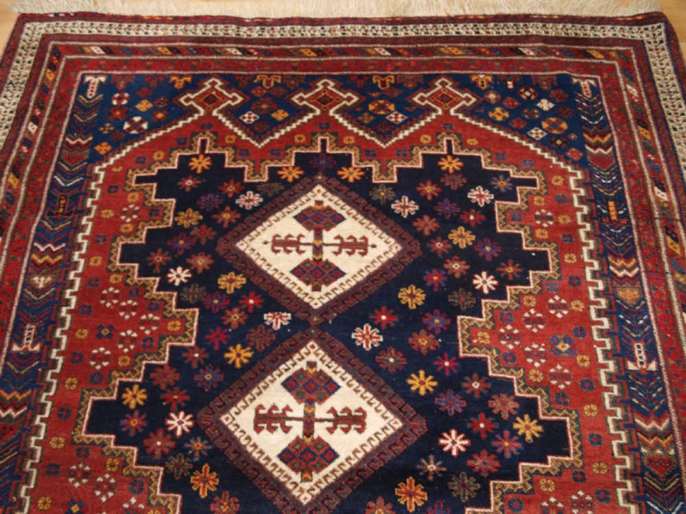 A hand-knotted antique Persian Afshar rug featuring three stacked diamond medallions surrounded by geometric floral motifs in navy blue, terracotta red, and ivory tones. View V