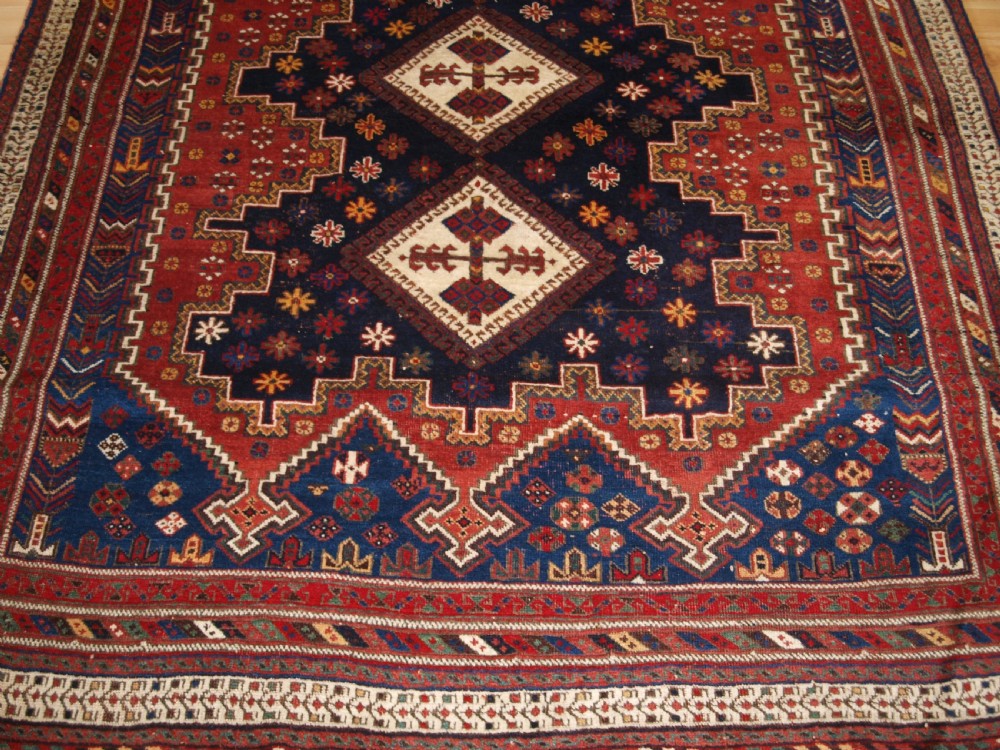 A hand-knotted antique Persian Afshar rug featuring three stacked diamond medallions surrounded by geometric floral motifs in navy blue, terracotta red, and ivory tones. View VII