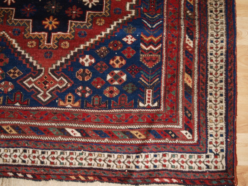 A hand-knotted antique Persian Afshar rug featuring three stacked diamond medallions surrounded by geometric floral motifs in navy blue, terracotta red, and ivory tones. View X