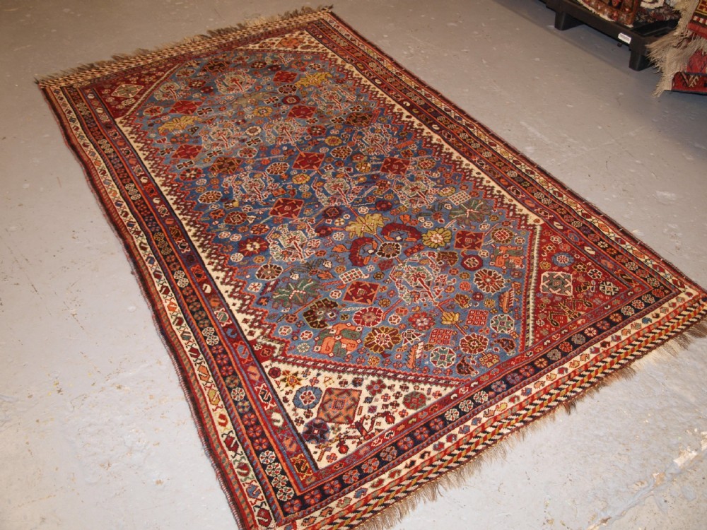 An antique hand-knotted Qashqai Persian rug featuring a central blue field filled with red, white, and yellow geometric tribal motifs framed by a multi-stripe border. View II