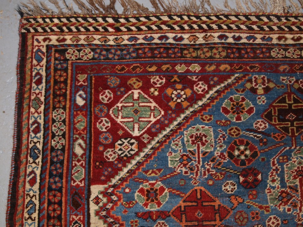 An antique hand-knotted Qashqai Persian rug featuring a central blue field filled with red, white, and yellow geometric tribal motifs framed by a multi-stripe border. View III