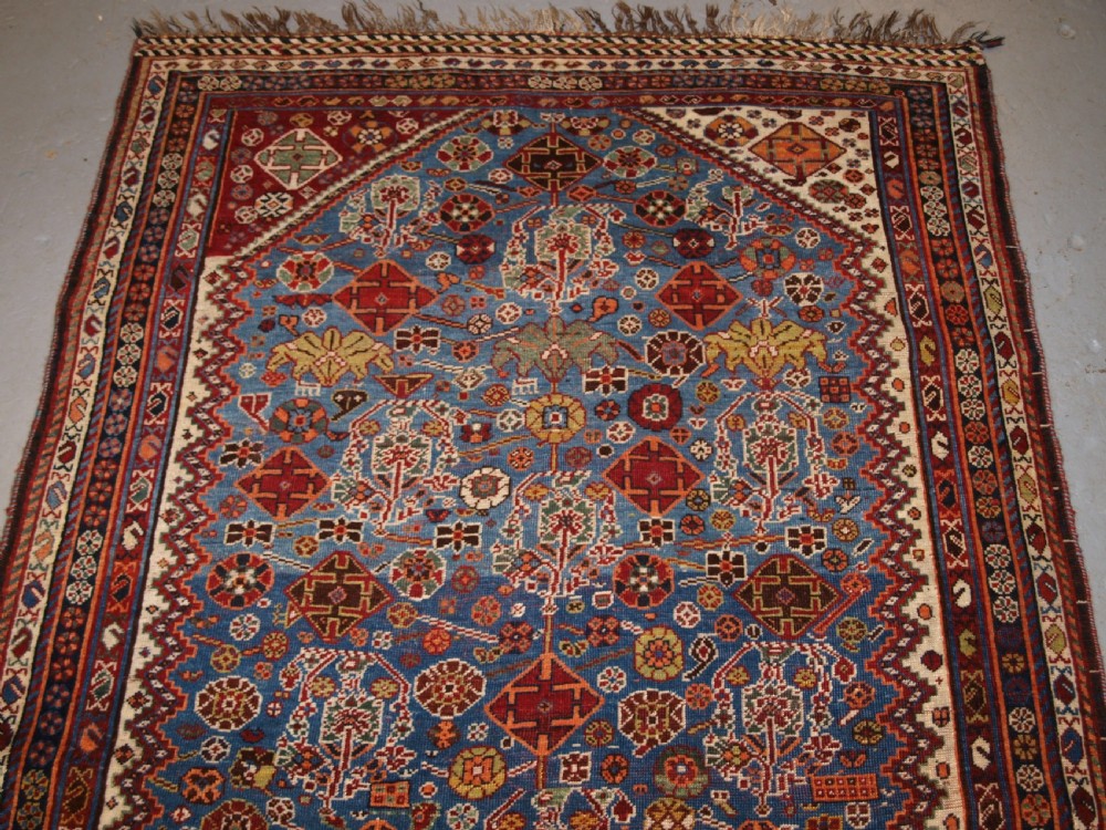 An antique hand-knotted Qashqai Persian rug featuring a central blue field filled with red, white, and yellow geometric tribal motifs framed by a multi-stripe border. View V