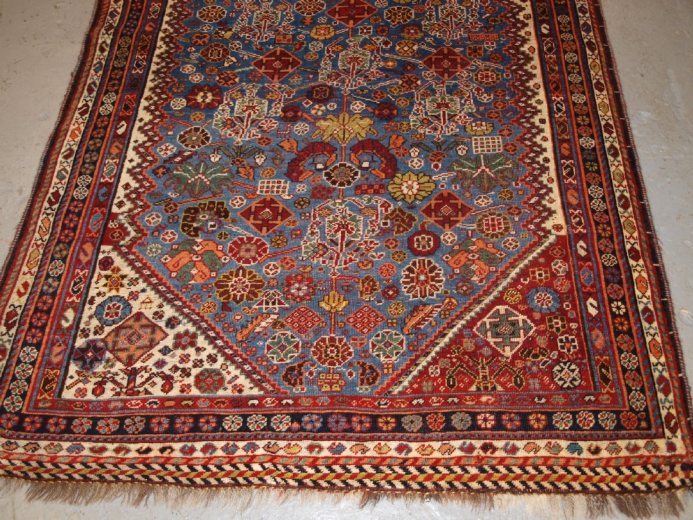 An antique hand-knotted Qashqai Persian rug featuring a central blue field filled with red, white, and yellow geometric tribal motifs framed by a multi-stripe border. View VII