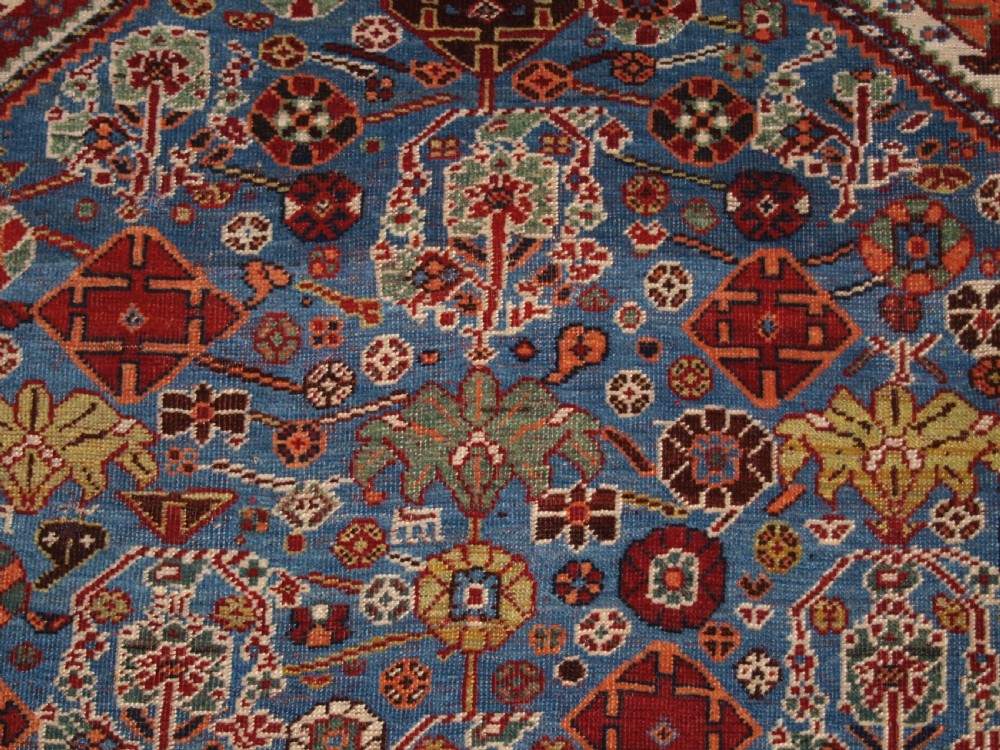 An antique hand-knotted Qashqai Persian rug featuring a central blue field filled with red, white, and yellow geometric tribal motifs framed by a multi-stripe border. View IX