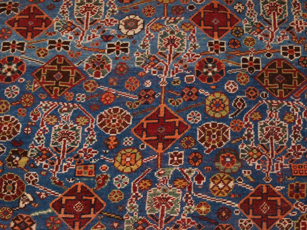 An antique hand-knotted Qashqai Persian rug featuring a central blue field filled with red, white, and yellow geometric tribal motifs framed by a multi-stripe border. View X