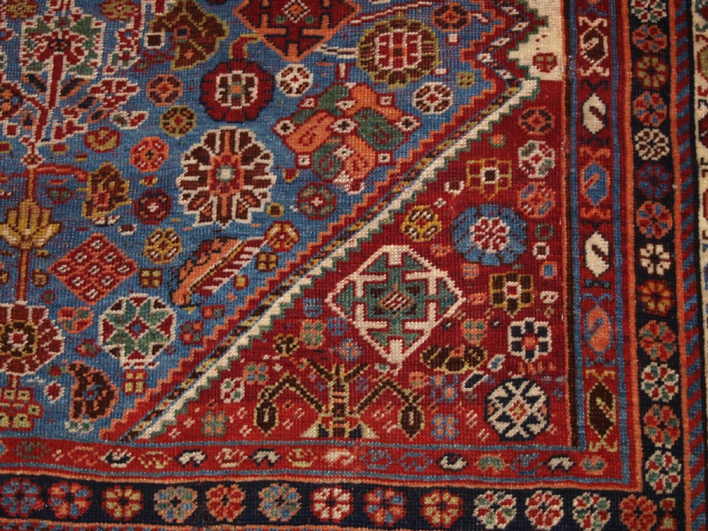 An antique hand-knotted Qashqai Persian rug featuring a central blue field filled with red, white, and yellow geometric tribal motifs framed by a multi-stripe border. View XI