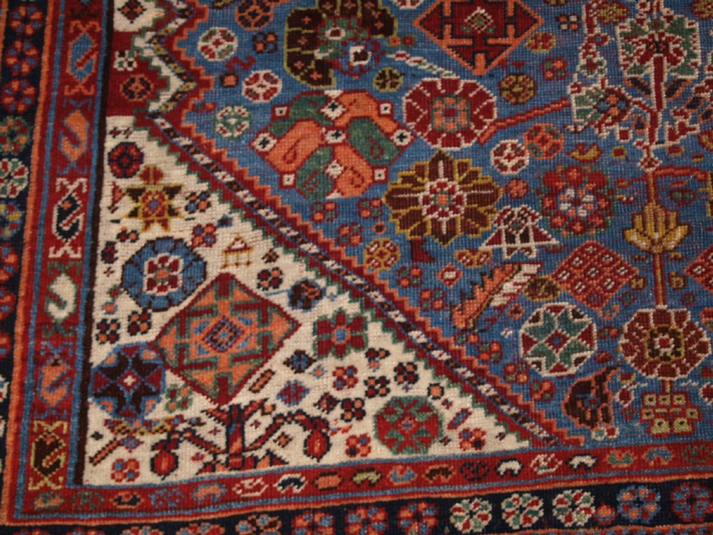 An antique hand-knotted Qashqai Persian rug featuring a central blue field filled with red, white, and yellow geometric tribal motifs framed by a multi-stripe border. View XII