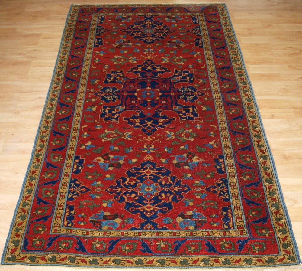 An antique hand-knotted Turkish Ushak carpet featuring a crimson red field decorated with large navy blue star medallions and detailed geometric borders.
