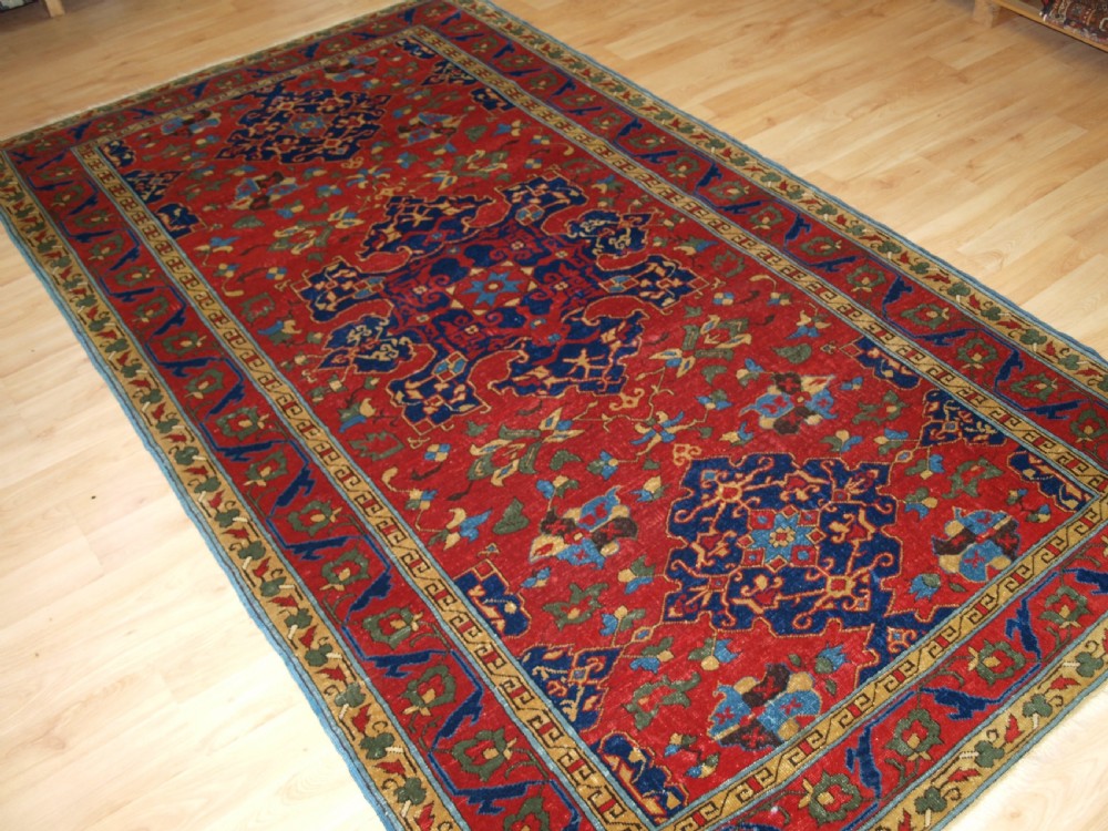 An antique hand-knotted Turkish Ushak carpet featuring a crimson red field decorated with large navy blue star medallions and detailed geometric borders. View II
