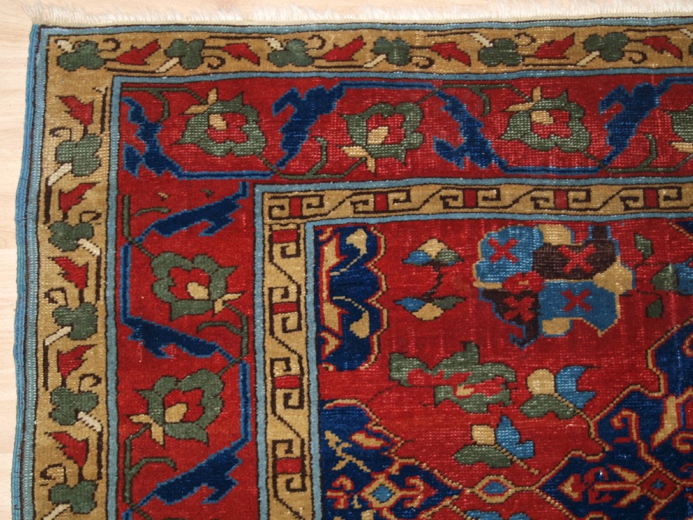 An antique hand-knotted Turkish Ushak carpet featuring a crimson red field decorated with large navy blue star medallions and detailed geometric borders. View III