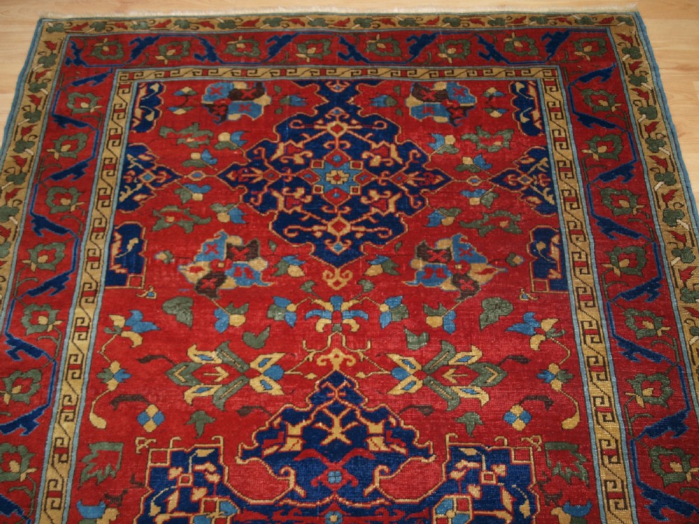 An antique hand-knotted Turkish Ushak carpet featuring a crimson red field decorated with large navy blue star medallions and detailed geometric borders. View IV