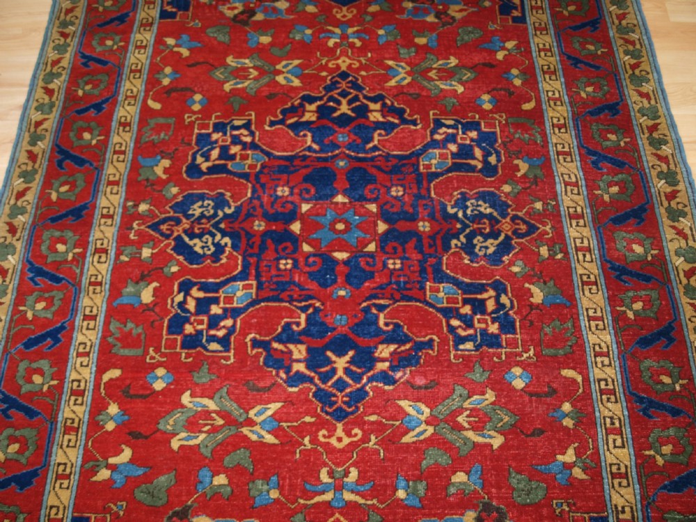 An antique hand-knotted Turkish Ushak carpet featuring a crimson red field decorated with large navy blue star medallions and detailed geometric borders. View V
