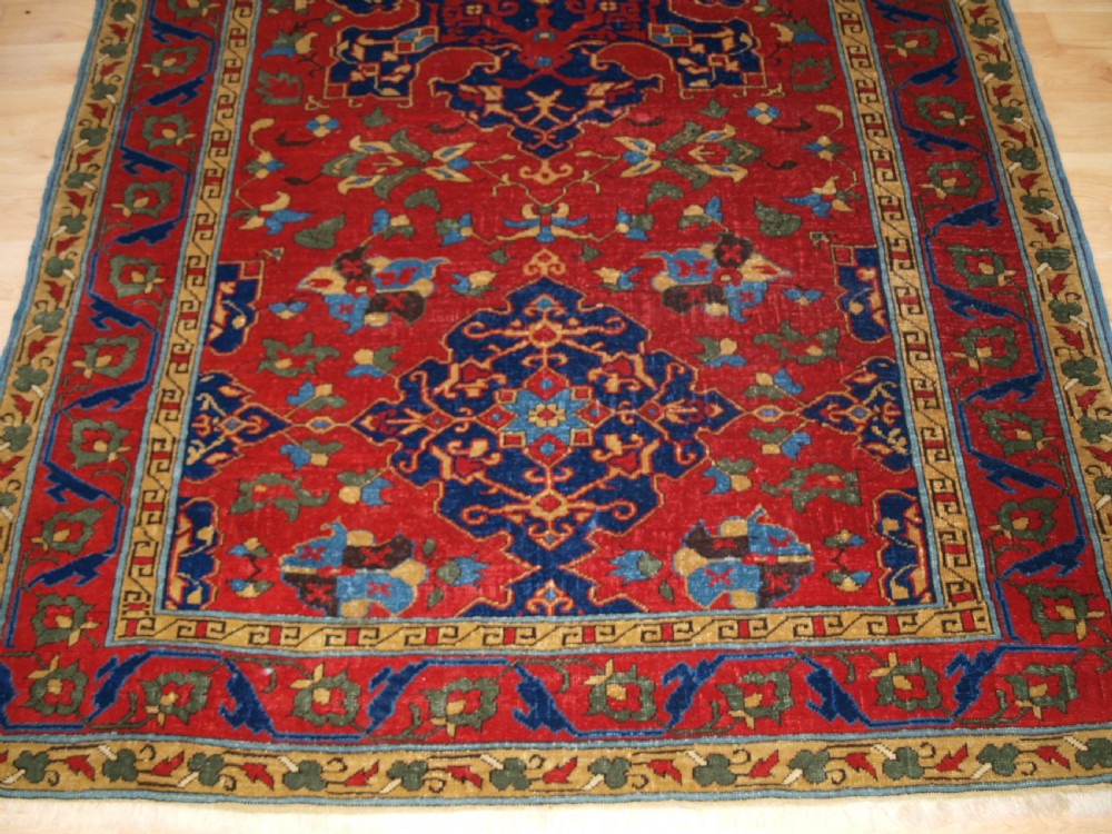 An antique hand-knotted Turkish Ushak carpet featuring a crimson red field decorated with large navy blue star medallions and detailed geometric borders. View VI