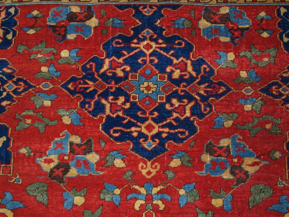 An antique hand-knotted Turkish Ushak carpet featuring a crimson red field decorated with large navy blue star medallions and detailed geometric borders. View VII