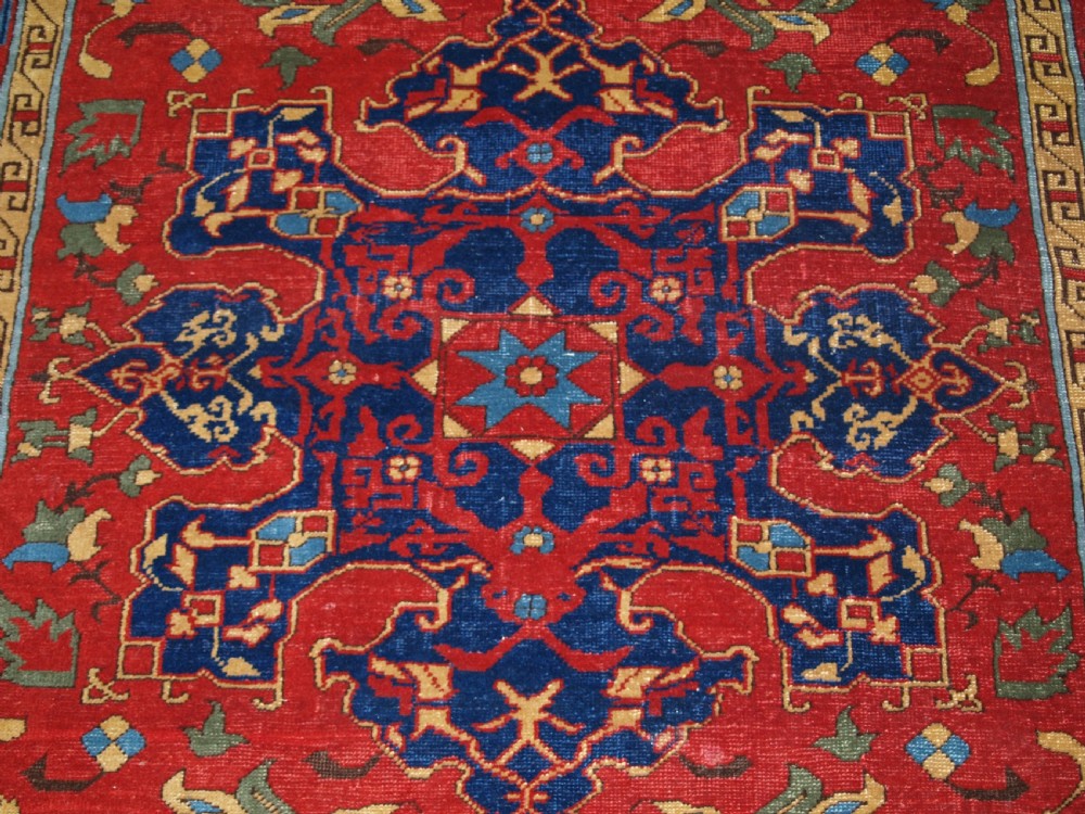 An antique hand-knotted Turkish Ushak carpet featuring a crimson red field decorated with large navy blue star medallions and detailed geometric borders. View VIII