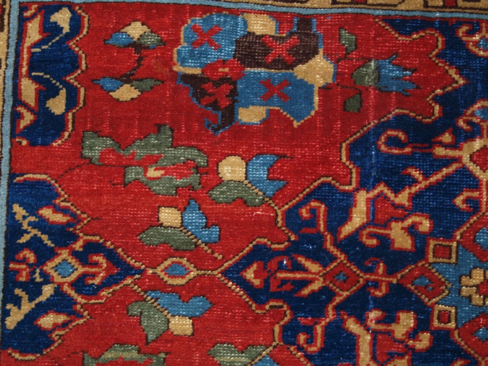 An antique hand-knotted Turkish Ushak carpet featuring a crimson red field decorated with large navy blue star medallions and detailed geometric borders. View X
