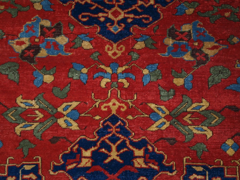 An antique hand-knotted Turkish Ushak carpet featuring a crimson red field decorated with large navy blue star medallions and detailed geometric borders. View XI