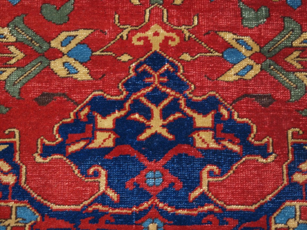 An antique hand-knotted Turkish Ushak carpet featuring a crimson red field decorated with large navy blue star medallions and detailed geometric borders. View XII
