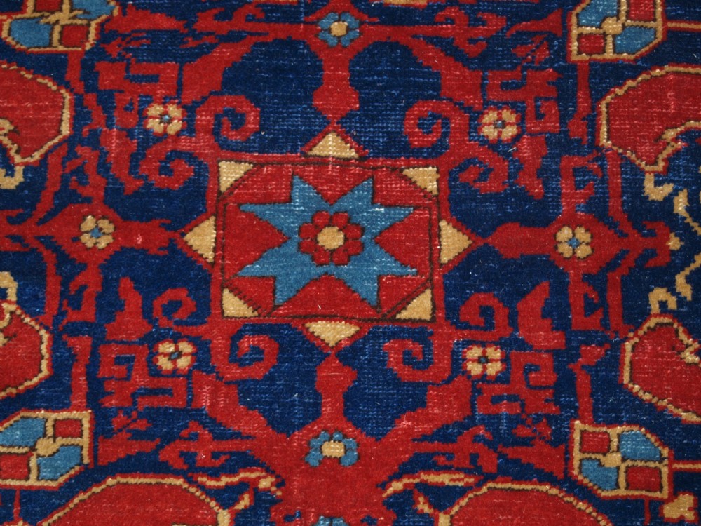 An antique hand-knotted Turkish Ushak carpet featuring a crimson red field decorated with large navy blue star medallions and detailed geometric borders. View XIII
