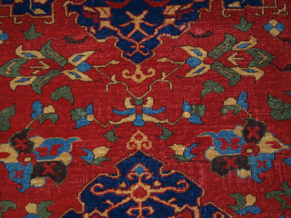 An antique hand-knotted Turkish Ushak carpet featuring a crimson red field decorated with large navy blue star medallions and detailed geometric borders. View XV