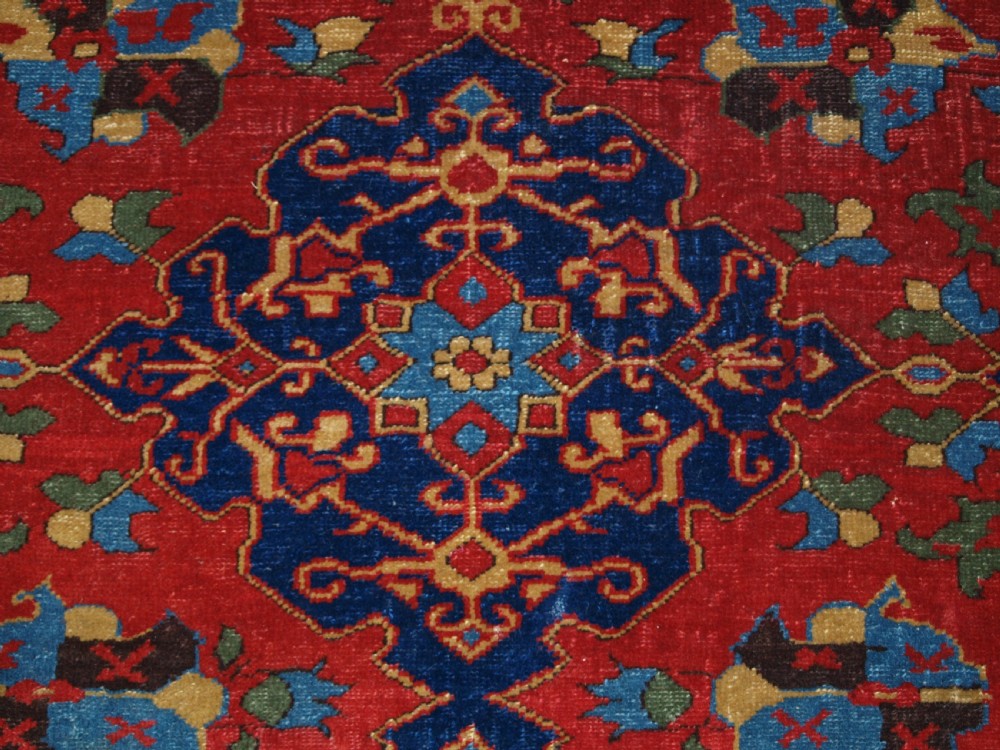 An antique hand-knotted Turkish Ushak carpet featuring a crimson red field decorated with large navy blue star medallions and detailed geometric borders. View XVI