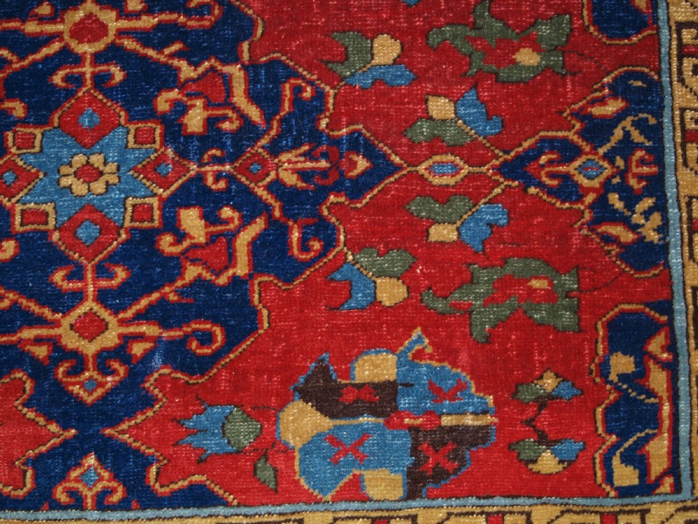 An antique hand-knotted Turkish Ushak carpet featuring a crimson red field decorated with large navy blue star medallions and detailed geometric borders. View XVII