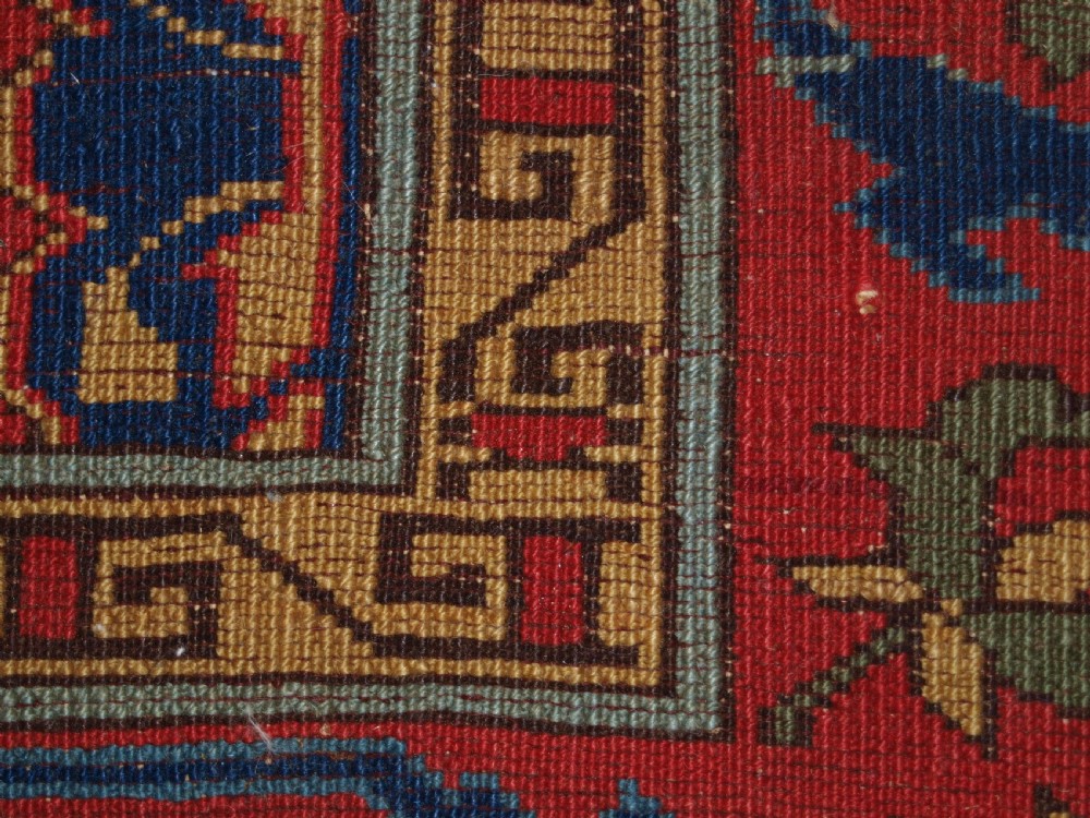 An antique hand-knotted Turkish Ushak carpet featuring a crimson red field decorated with large navy blue star medallions and detailed geometric borders. View XIX