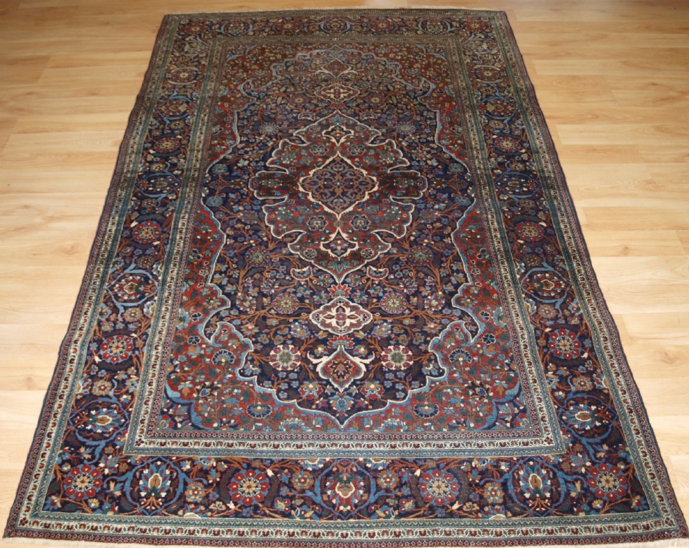 A hand-knotted Persian Kork Kashan wool rug featuring a central medallion with intricate floral motifs in navy blue, red, and cream.