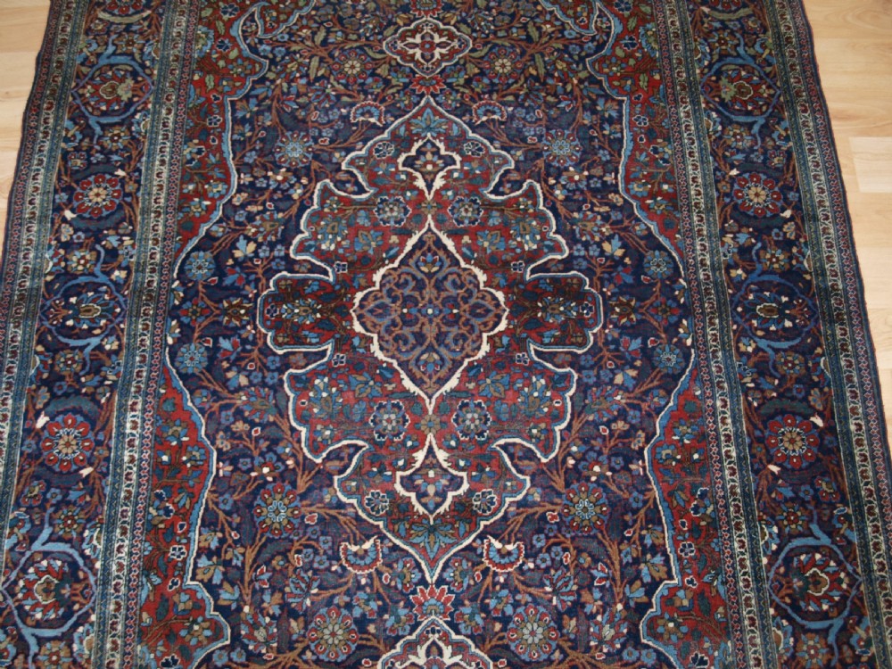 A hand-knotted Persian Kork Kashan wool rug featuring a central medallion with intricate floral motifs in navy blue, red, and cream. View V