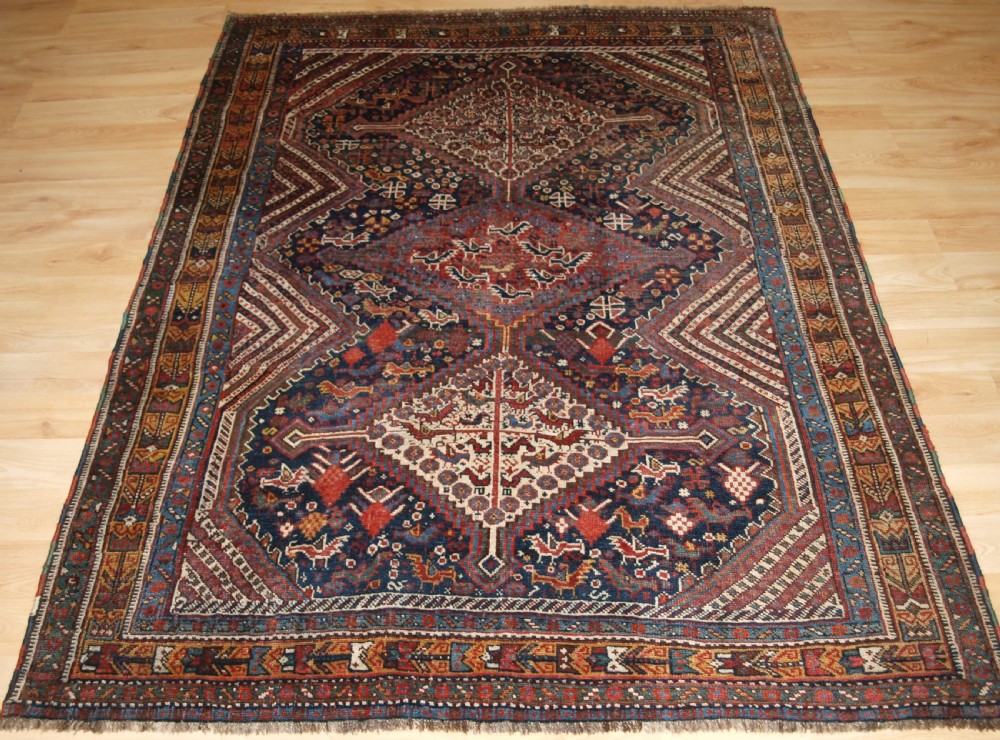 An antique hand-knotted Persian Khamseh wool rug featuring triple diamond medallions filled with stylized bird motifs on a dark navy and red geometric field.
