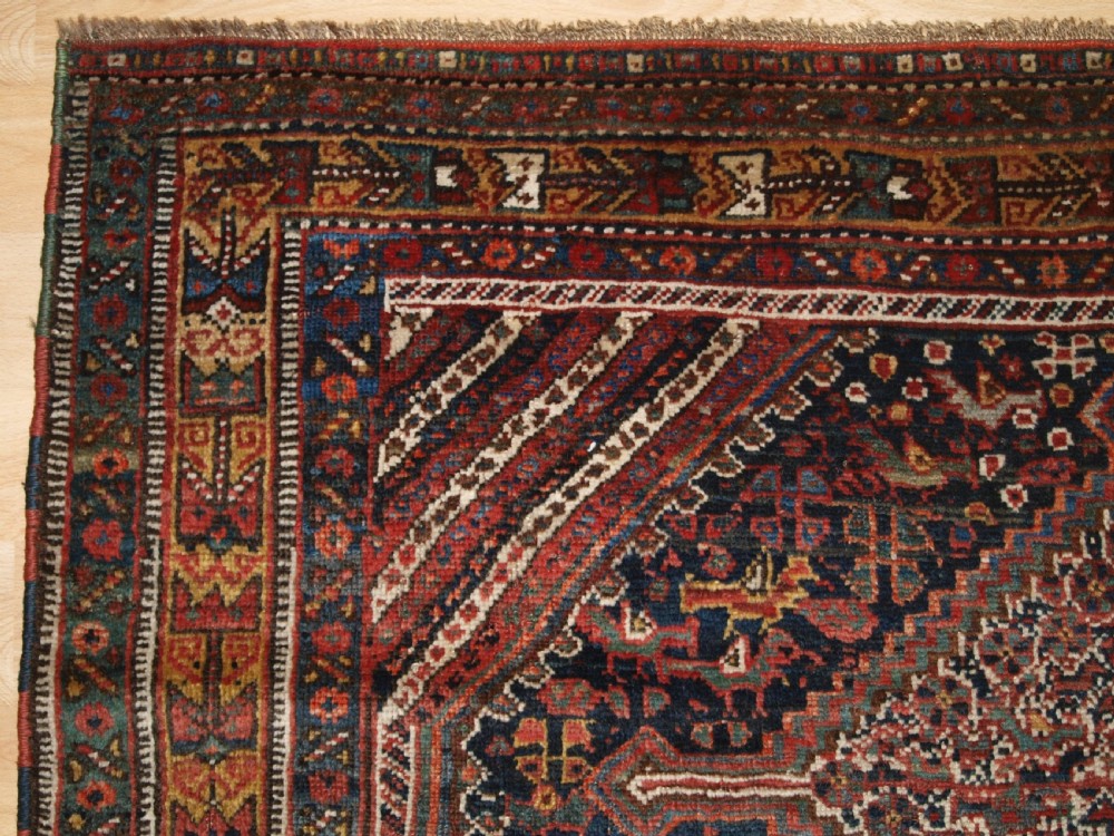 An antique hand-knotted Persian Khamseh wool rug featuring triple diamond medallions filled with stylized bird motifs on a dark navy and red geometric field. View III