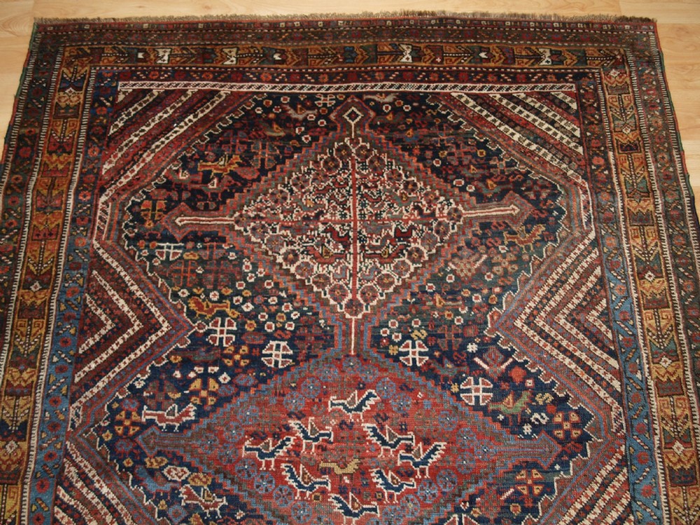 An antique hand-knotted Persian Khamseh wool rug featuring triple diamond medallions filled with stylized bird motifs on a dark navy and red geometric field. View IV