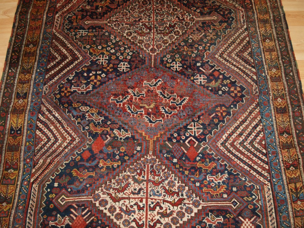 An antique hand-knotted Persian Khamseh wool rug featuring triple diamond medallions filled with stylized bird motifs on a dark navy and red geometric field. View V