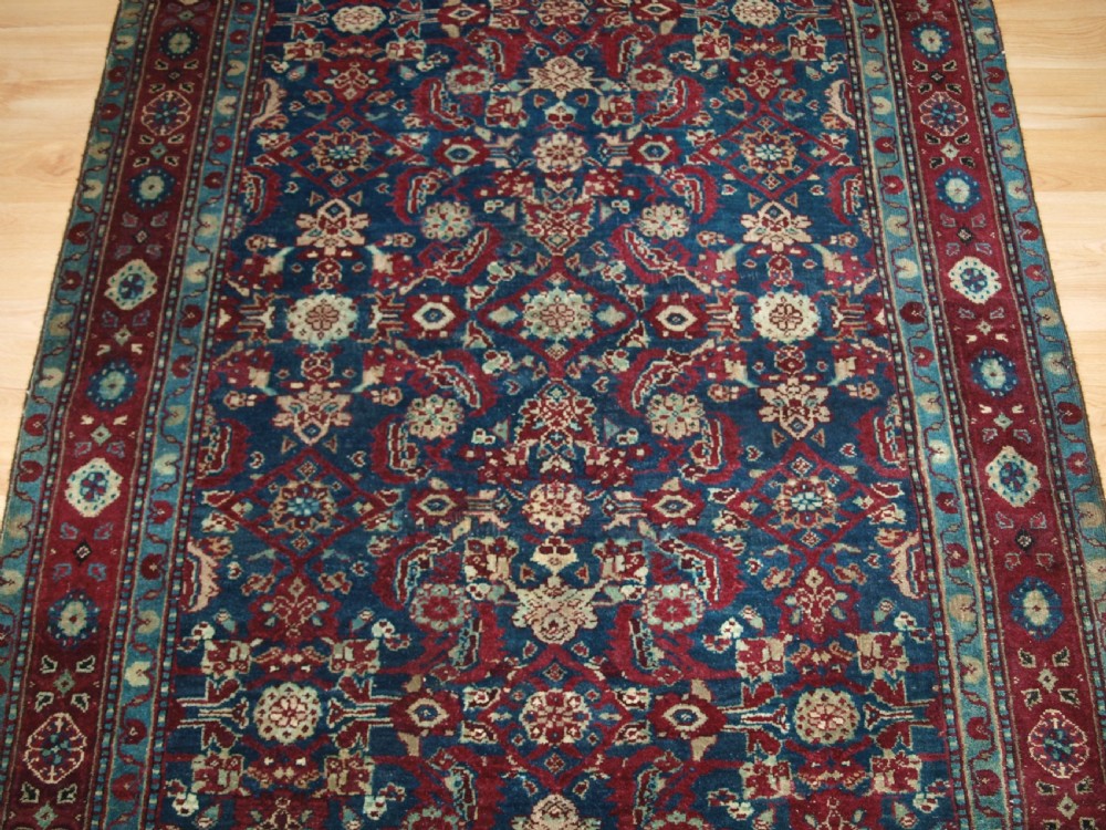 A late 19th-century hand-knotted Indian Agra carpet featuring an intricate all-over floral pattern on a deep blue field with a wide crimson border. View V