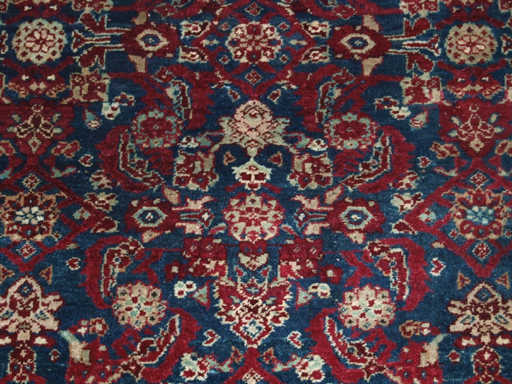 A late 19th-century hand-knotted Indian Agra carpet featuring an intricate all-over floral pattern on a deep blue field with a wide crimson border. View X