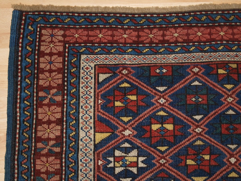 An antique hand-knotted Caucasian rug featuring a central navy blue field with a geometric star-and-lattice pattern framed by a reddish-pink patterned border. View III