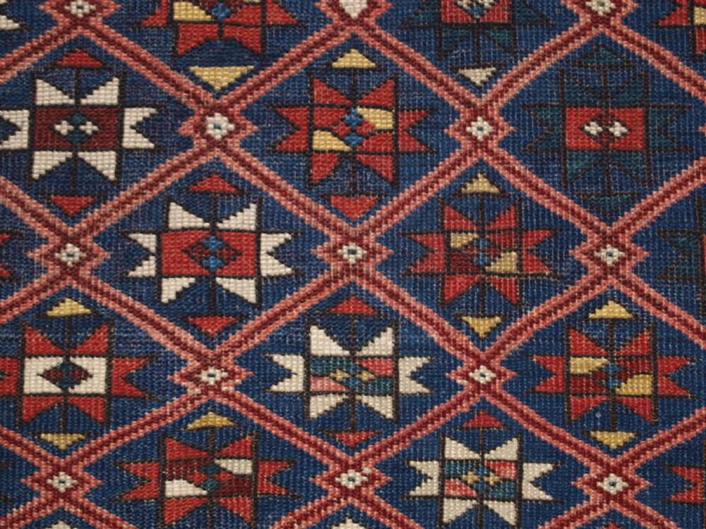 An antique hand-knotted Caucasian rug featuring a central navy blue field with a geometric star-and-lattice pattern framed by a reddish-pink patterned border. View VIII