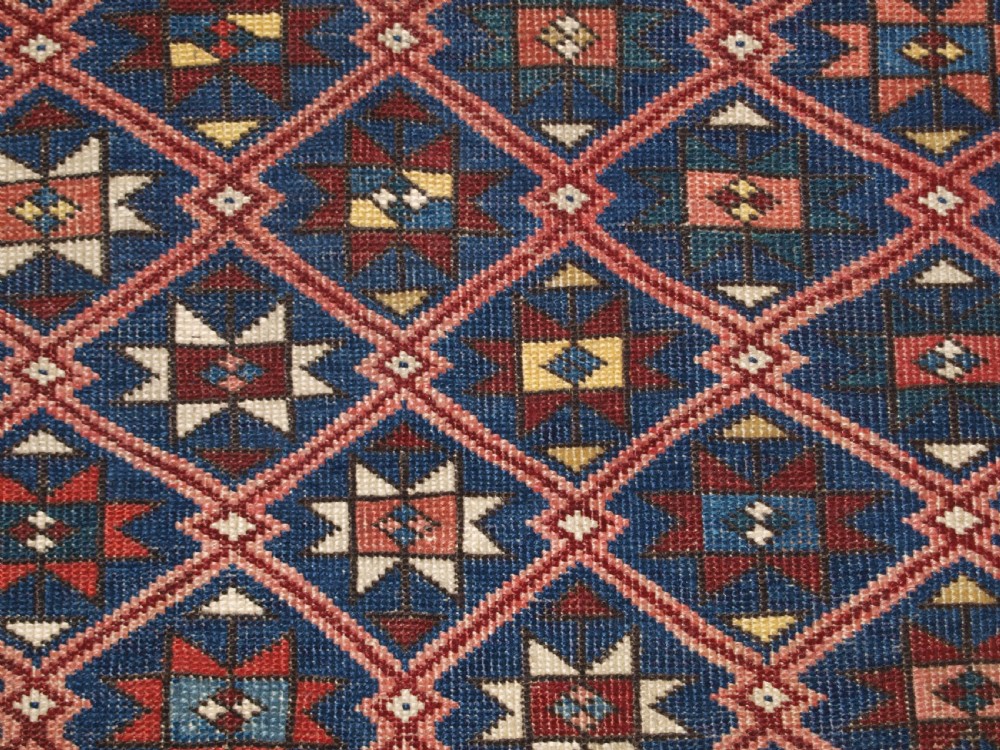 An antique hand-knotted Caucasian rug featuring a central navy blue field with a geometric star-and-lattice pattern framed by a reddish-pink patterned border. View IX