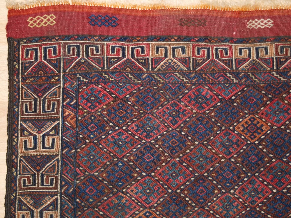A long handwoven rectangular Kurdish Soumak kilim rug featuring a dense red and blue diamond lattice pattern framed by a geometric meander border. View III