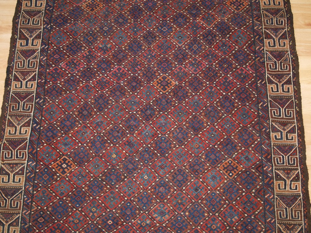 A long handwoven rectangular Kurdish Soumak kilim rug featuring a dense red and blue diamond lattice pattern framed by a geometric meander border. View V