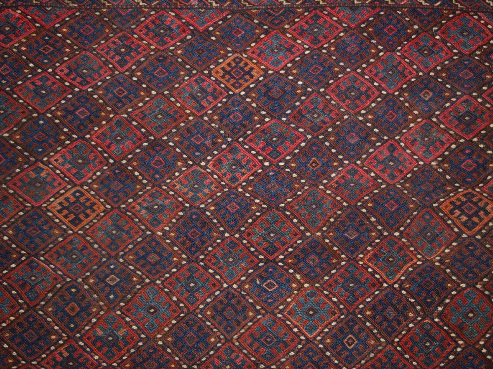 A long handwoven rectangular Kurdish Soumak kilim rug featuring a dense red and blue diamond lattice pattern framed by a geometric meander border. View VII