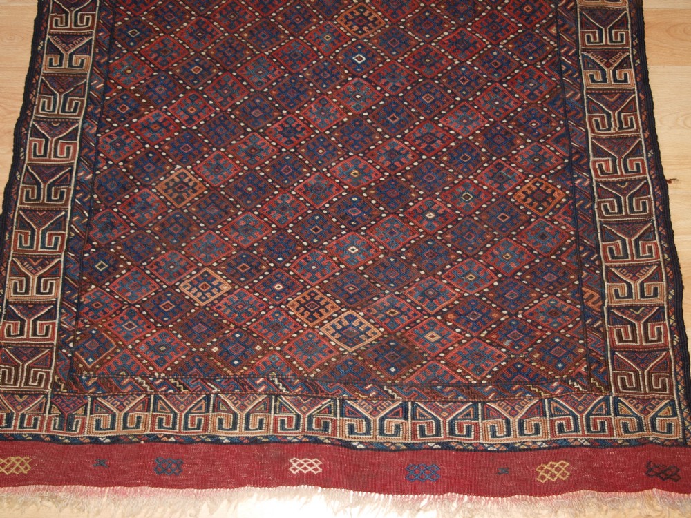 A long handwoven rectangular Kurdish Soumak kilim rug featuring a dense red and blue diamond lattice pattern framed by a geometric meander border. View VIII