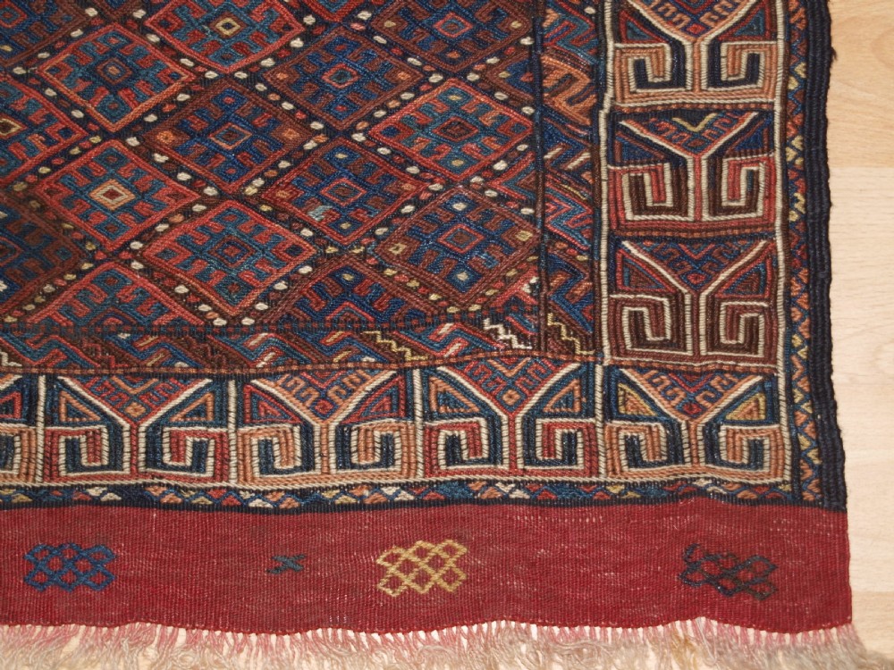 A long handwoven rectangular Kurdish Soumak kilim rug featuring a dense red and blue diamond lattice pattern framed by a geometric meander border. View IX