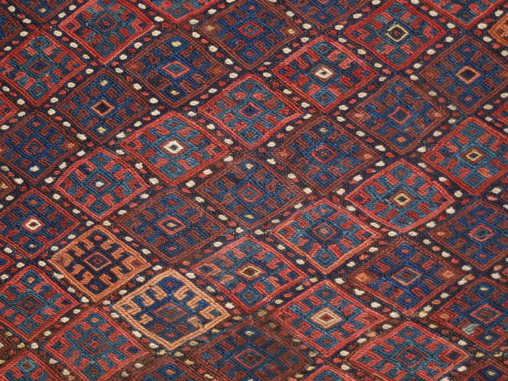 A long handwoven rectangular Kurdish Soumak kilim rug featuring a dense red and blue diamond lattice pattern framed by a geometric meander border. View X