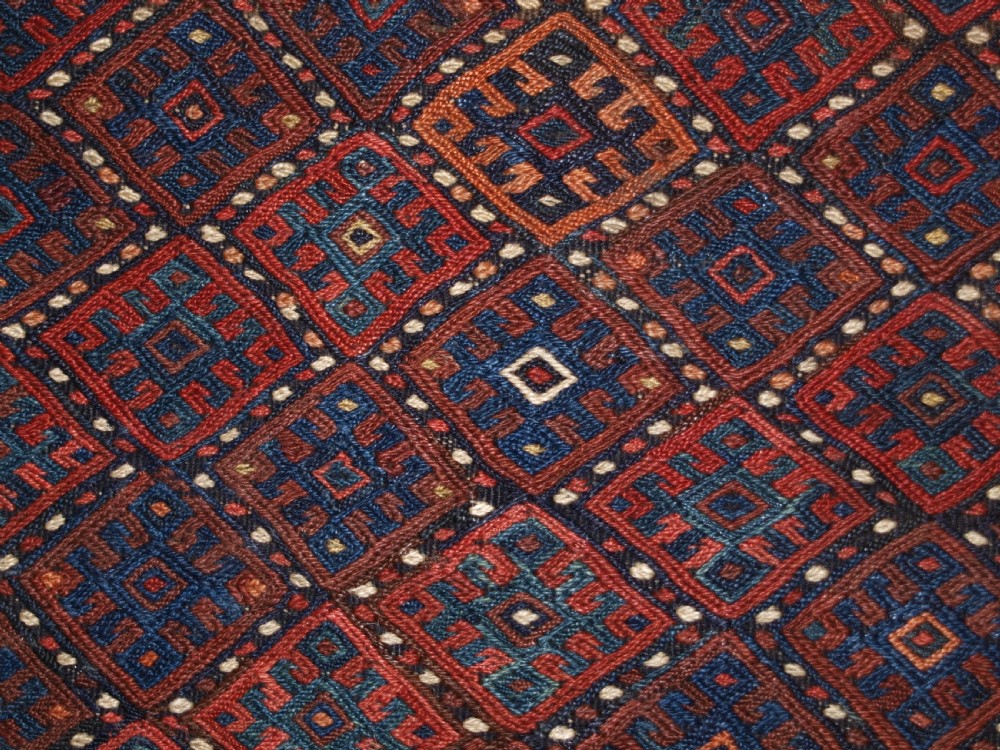 A long handwoven rectangular Kurdish Soumak kilim rug featuring a dense red and blue diamond lattice pattern framed by a geometric meander border. View XI