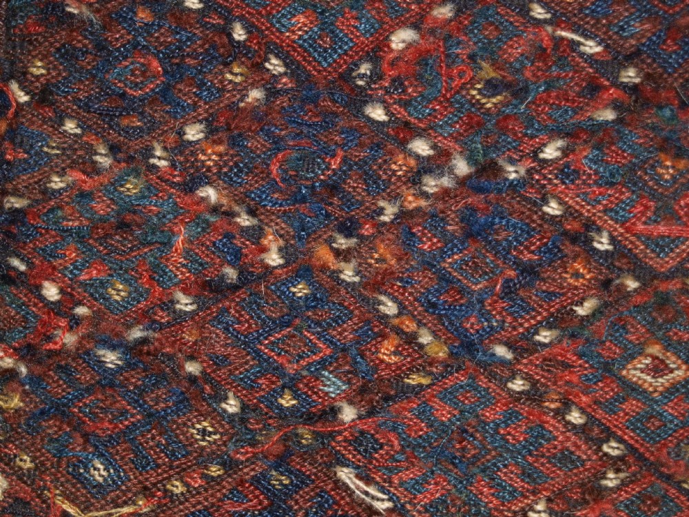 A long handwoven rectangular Kurdish Soumak kilim rug featuring a dense red and blue diamond lattice pattern framed by a geometric meander border. View XII