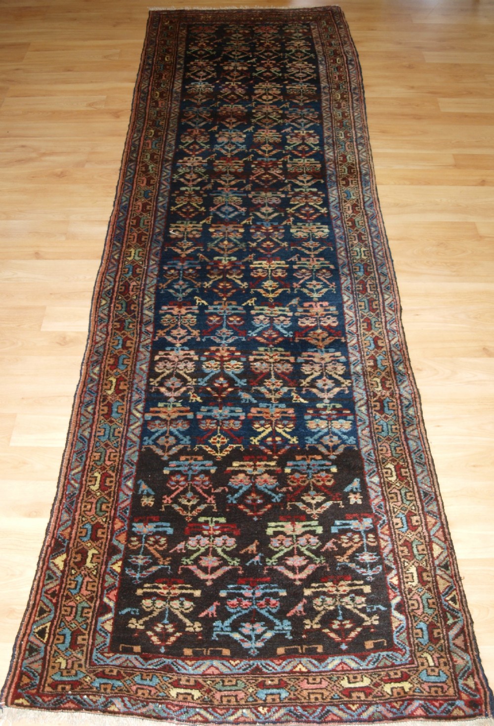 A long narrow antique Luri wool runner carpet with repeating colourful geometric tribal motifs on a dark indigo background framed by decorative multi-band borders.