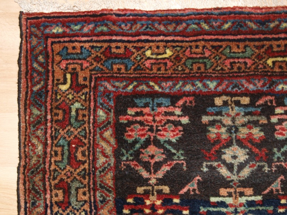 A long narrow antique Luri wool runner carpet with repeating colourful geometric tribal motifs on a dark indigo background framed by decorative multi-band borders. View II