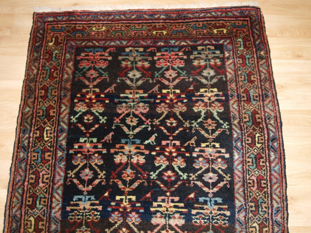 A long narrow antique Luri wool runner carpet with repeating colourful geometric tribal motifs on a dark indigo background framed by decorative multi-band borders. View IV